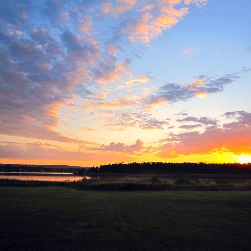 Sunrise over Cedarville Bay, with the wooded Les Cheneaux Islands silhouetted along the horizon and colour reflecting off still water.